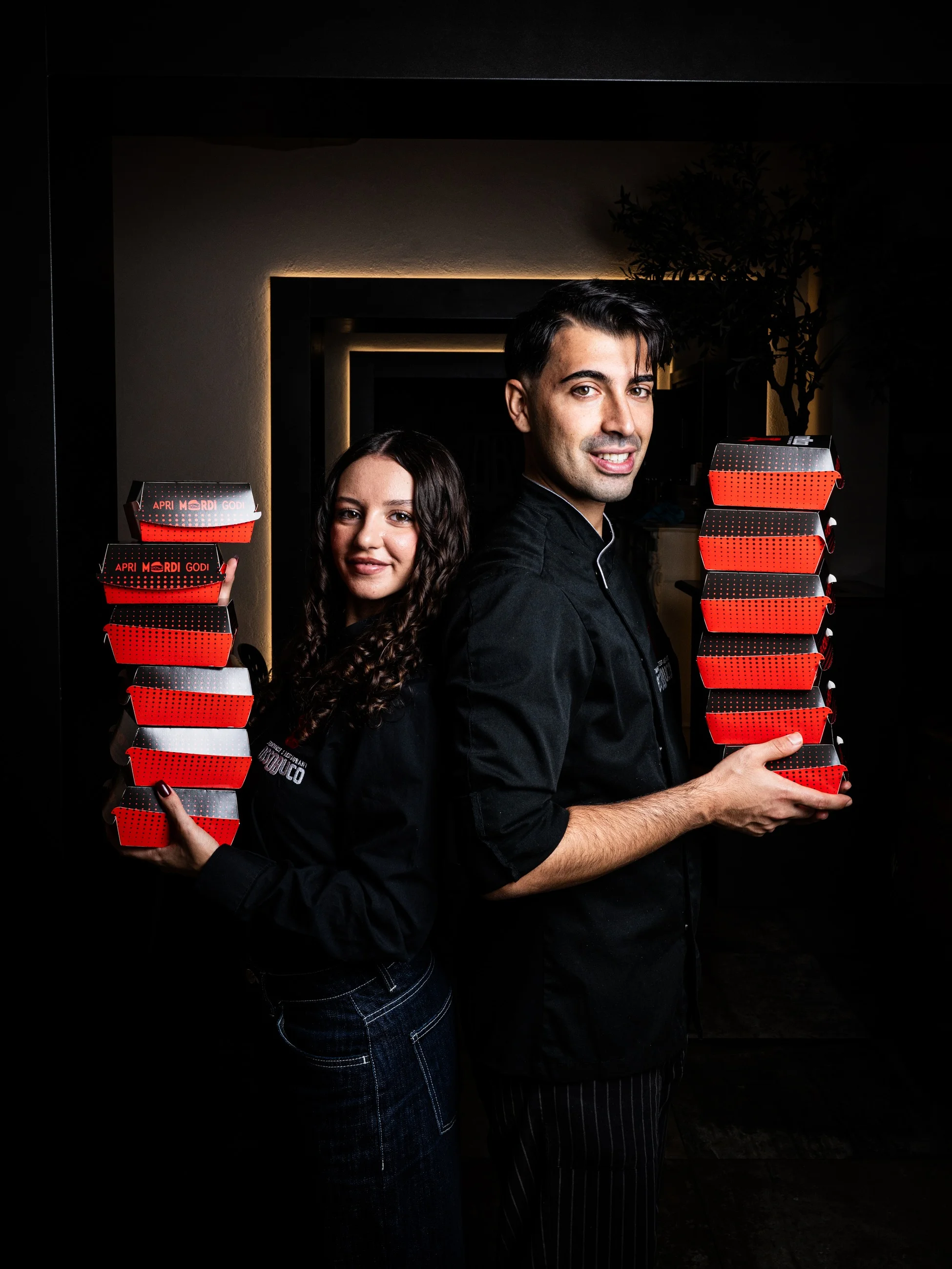 Emanuele and Francesca, founders of Ossobuco, holding stacks of red takeaway boxes